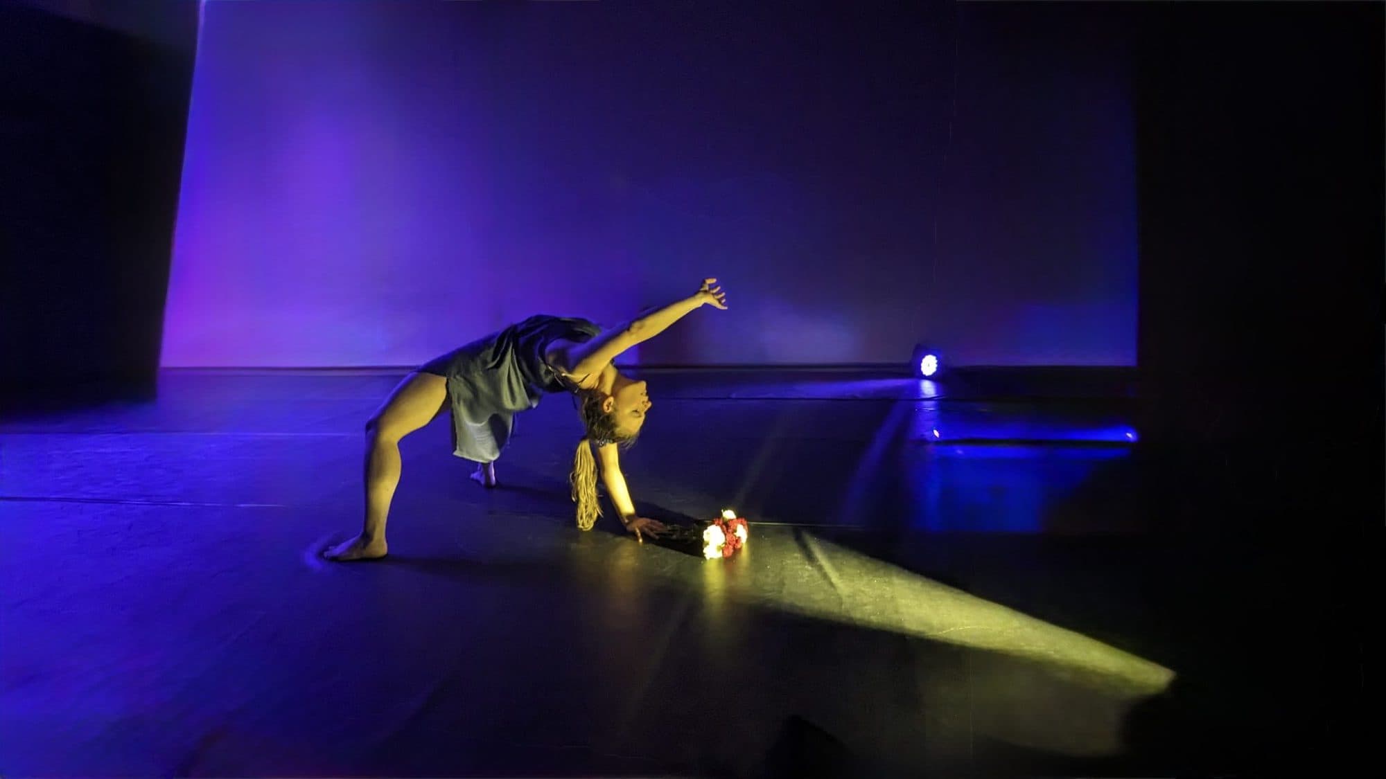 Laura on a blue-lit stage beside a small lamp