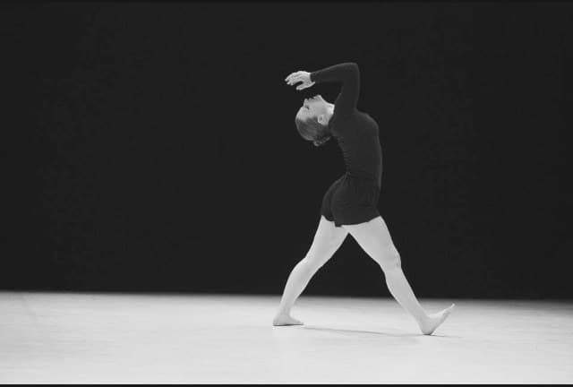 Laura in black on a bare stage, arm arched over her head