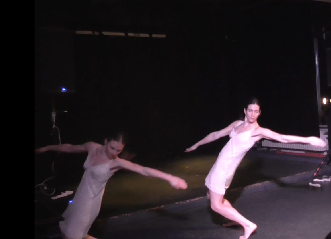 Two dancers in white slips on a dark stage